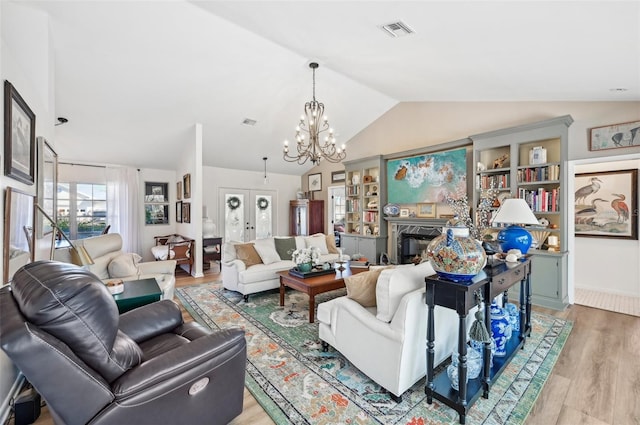 living room with lofted ceiling, a chandelier, light hardwood / wood-style floors, and french doors