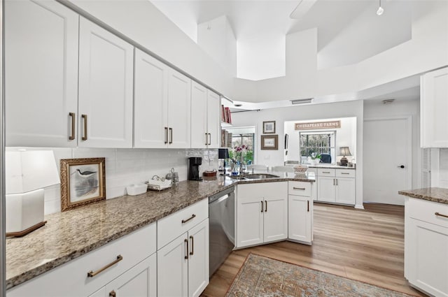 kitchen featuring a towering ceiling, dishwasher, white cabinetry, light hardwood / wood-style floors, and dark stone countertops