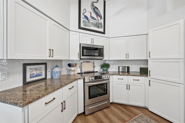 kitchen featuring decorative backsplash, appliances with stainless steel finishes, white cabinetry, light wood-type flooring, and dark stone countertops