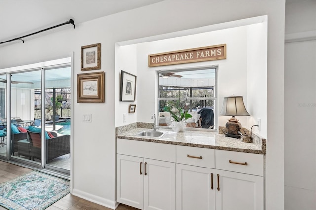 bar with white cabinetry, sink, wood-type flooring, and light stone counters