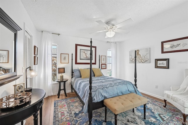 bedroom featuring a textured ceiling, ceiling fan, multiple windows, and hardwood / wood-style flooring