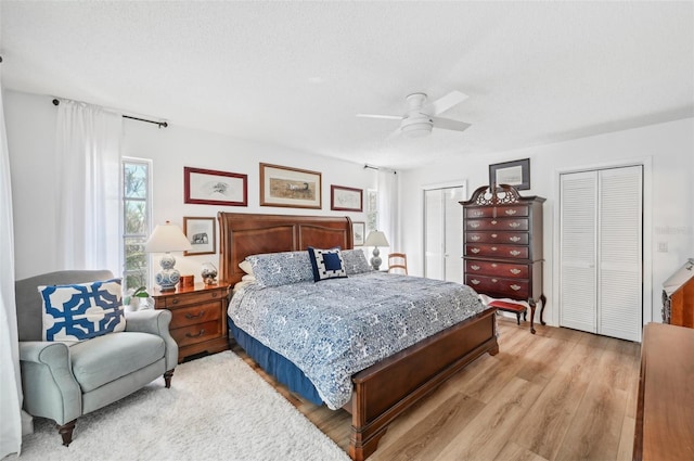 bedroom with a textured ceiling, two closets, light wood-type flooring, and ceiling fan