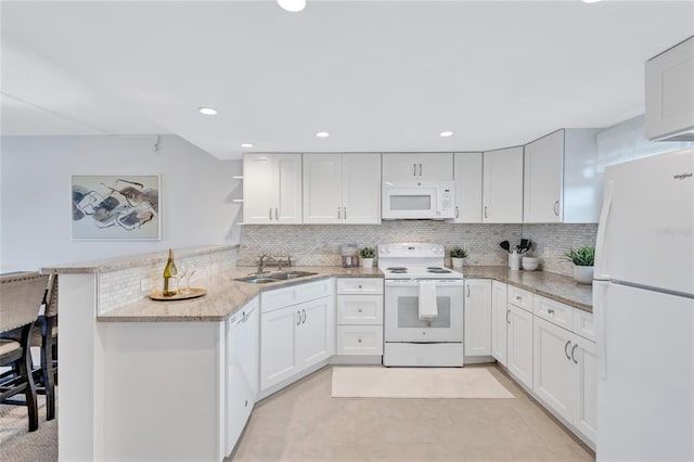 kitchen with kitchen peninsula, a breakfast bar area, white appliances, white cabinets, and decorative backsplash