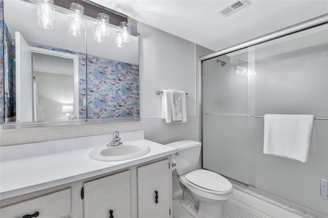 bathroom featuring a shower with door, tile patterned flooring, vanity, toilet, and tile walls