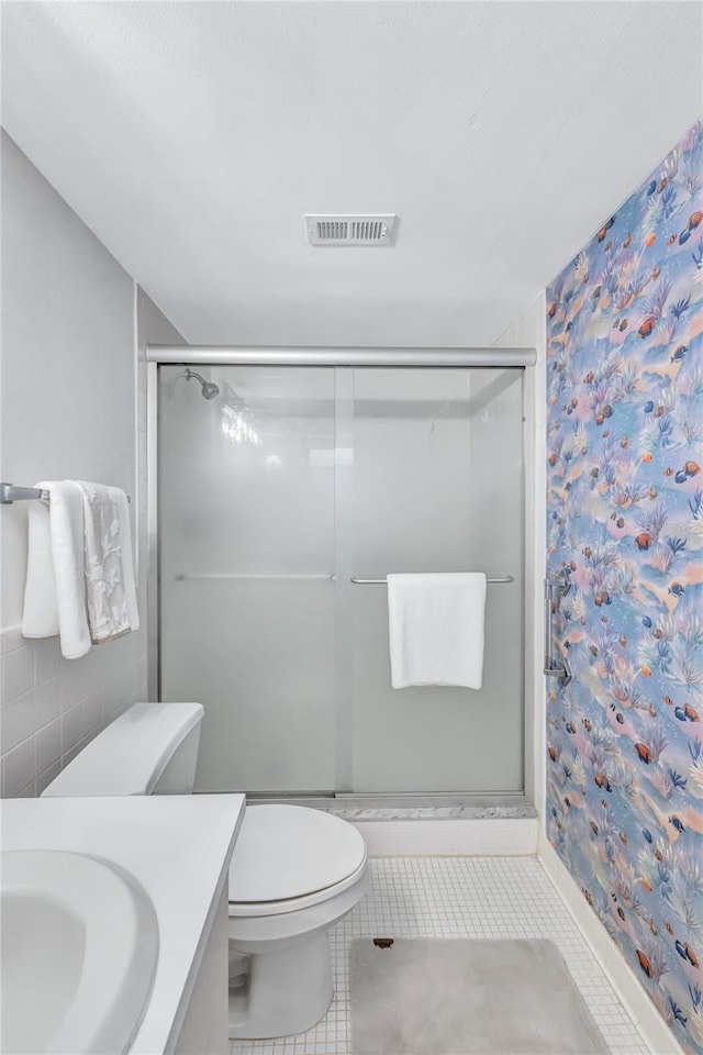 bathroom featuring toilet, vanity, tile patterned flooring, and a shower with door