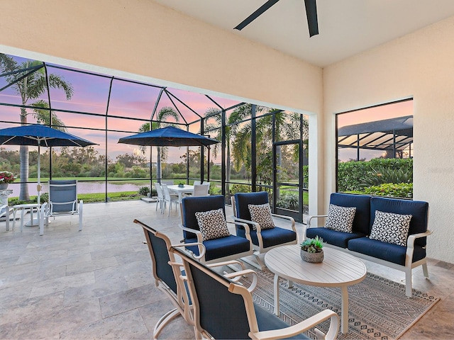 patio terrace at dusk featuring a lanai, a water view, an outdoor living space, and ceiling fan