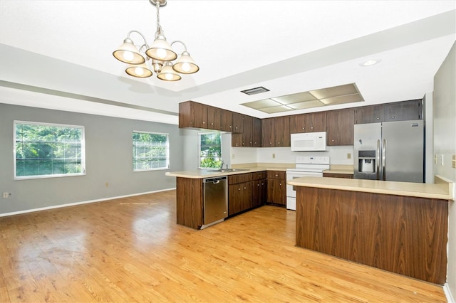 kitchen featuring kitchen peninsula, appliances with stainless steel finishes, hanging light fixtures, a chandelier, and light hardwood / wood-style flooring