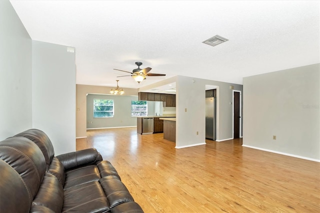 living room with light hardwood / wood-style floors, ceiling fan with notable chandelier, and a textured ceiling