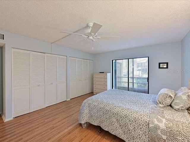 bedroom featuring a textured ceiling, two closets, hardwood / wood-style flooring, and ceiling fan