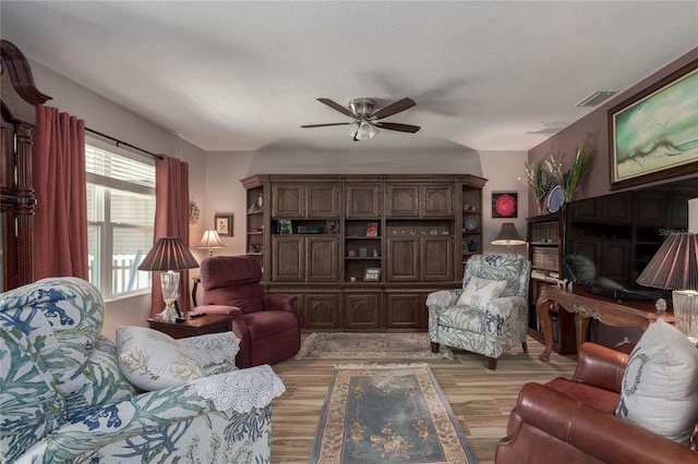 living room with light hardwood / wood-style flooring, a textured ceiling, and ceiling fan