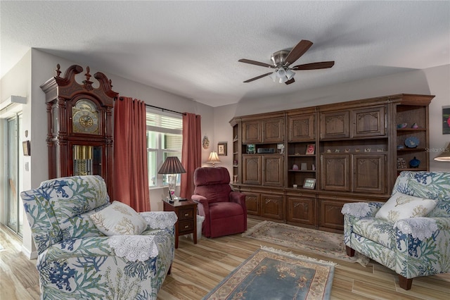 living area featuring a textured ceiling, light wood-type flooring, and ceiling fan