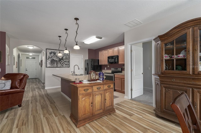 kitchen with black appliances, a textured ceiling, light hardwood / wood-style floors, decorative light fixtures, and a kitchen island with sink