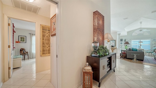 corridor with lofted ceiling, light tile patterned flooring, and a textured ceiling