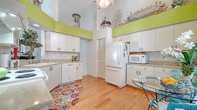 kitchen featuring a towering ceiling, white cabinetry, light wood-type flooring, and white appliances