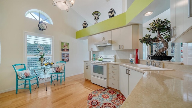 kitchen with high vaulted ceiling, electric range, plenty of natural light, and white cabinets