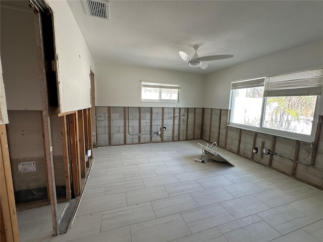 empty room with ceiling fan, a textured ceiling, and tile walls