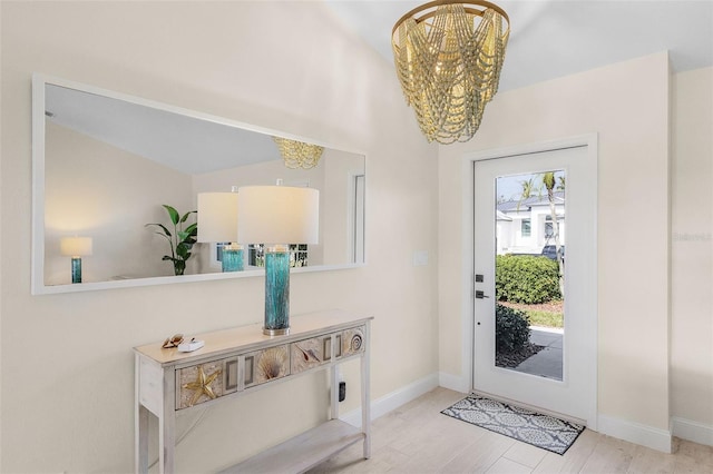 entryway with lofted ceiling, an inviting chandelier, and light wood-type flooring