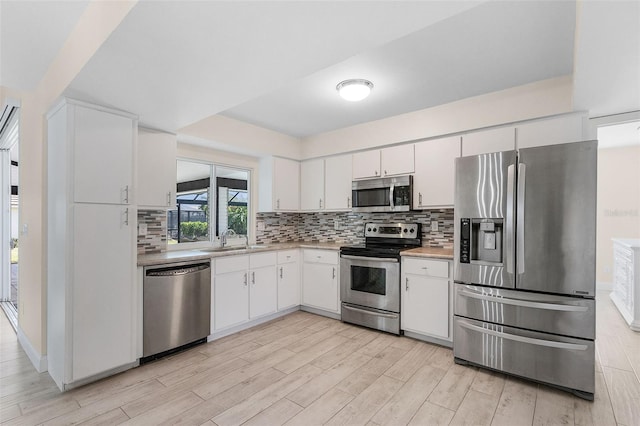 kitchen featuring white cabinets, backsplash, light hardwood / wood-style flooring, sink, and stainless steel appliances