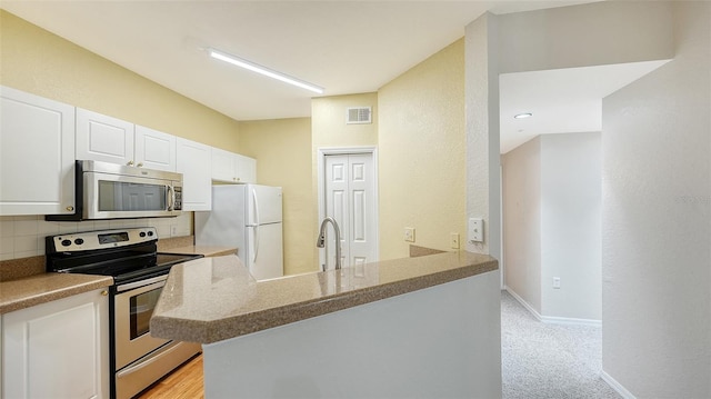 kitchen featuring decorative backsplash, kitchen peninsula, stainless steel appliances, light carpet, and white cabinetry