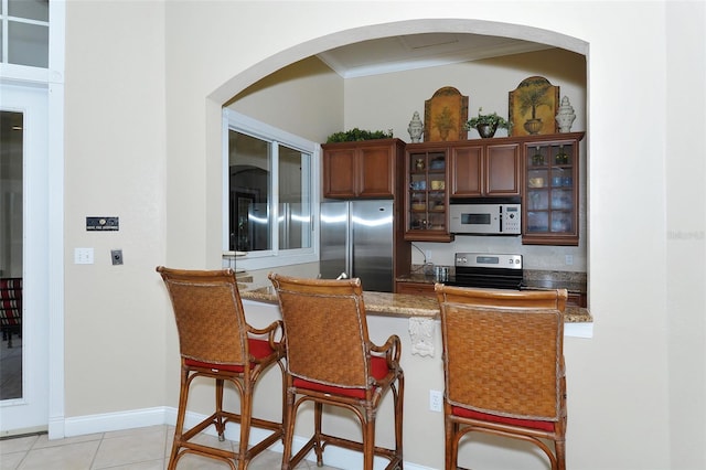 kitchen with ornamental molding, light stone countertops, light tile patterned flooring, range, and stainless steel refrigerator