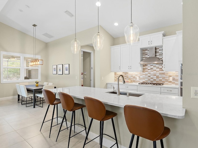 kitchen featuring pendant lighting, backsplash, wall chimney range hood, sink, and white cabinetry