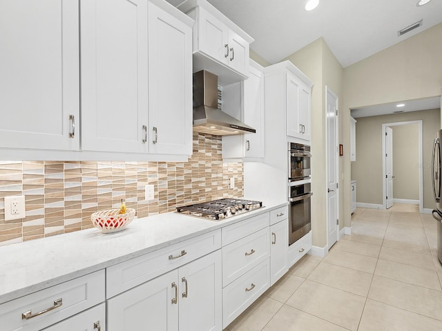 kitchen featuring white cabinetry, wall chimney range hood, light stone counters, backsplash, and appliances with stainless steel finishes