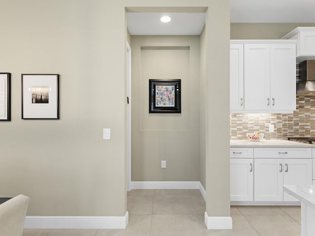 kitchen featuring white cabinets, wall chimney range hood, light tile patterned floors, and tasteful backsplash