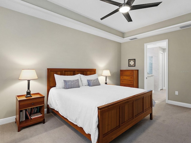 bedroom with a raised ceiling, ceiling fan, light colored carpet, and connected bathroom