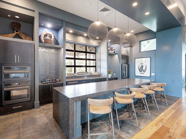 kitchen with a center island, sink, double oven, pendant lighting, and a kitchen bar