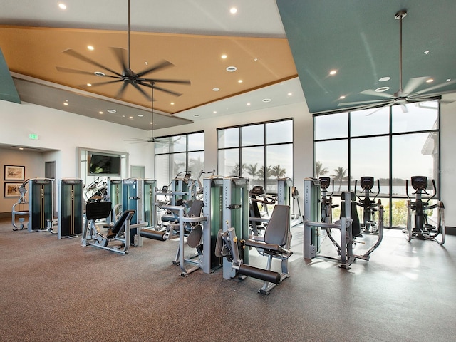 gym with ceiling fan, a wall of windows, and a high ceiling