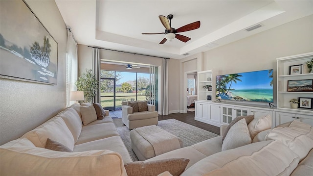 living room featuring ceiling fan, a tray ceiling, and hardwood / wood-style floors