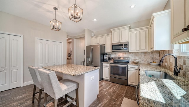 kitchen featuring sink, a center island, stainless steel appliances, decorative light fixtures, and dark wood-type flooring