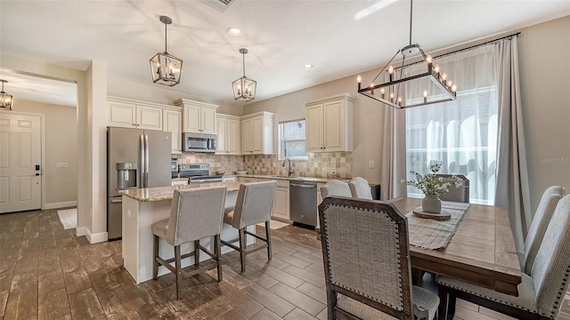 kitchen featuring dark hardwood / wood-style flooring, a kitchen island, light stone countertops, stainless steel appliances, and decorative light fixtures