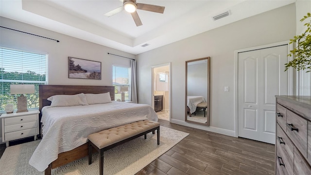 bedroom featuring connected bathroom, dark wood-type flooring, a tray ceiling, and ceiling fan