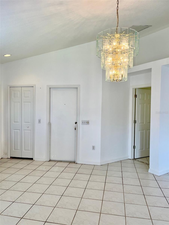 empty room with a notable chandelier, light tile patterned floors, and vaulted ceiling