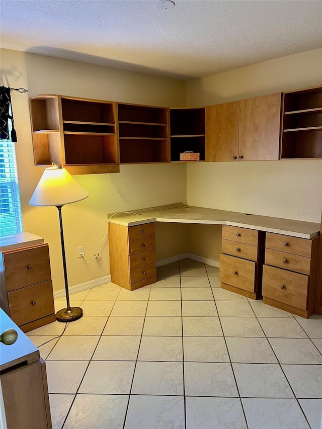 unfurnished office with built in desk, light tile patterned flooring, and a textured ceiling