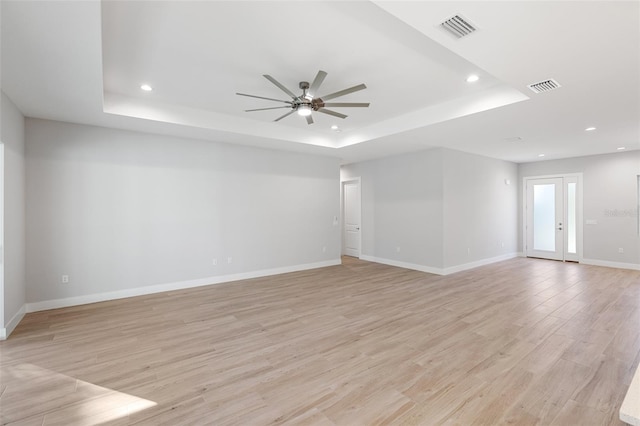 spare room with ceiling fan, light wood-type flooring, and a raised ceiling