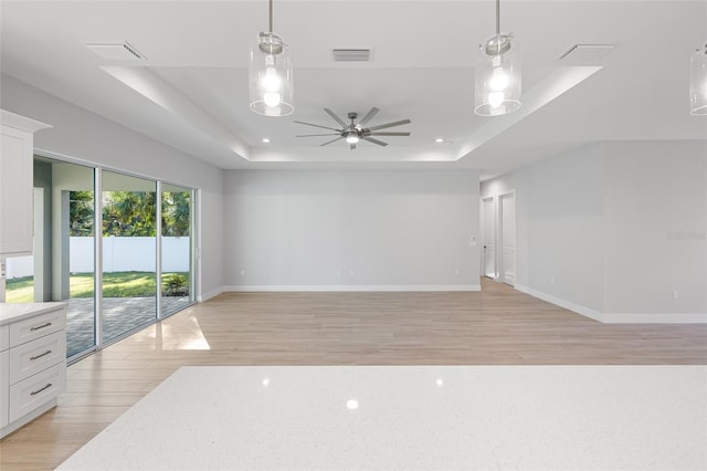 unfurnished room featuring ceiling fan, light wood-type flooring, and a raised ceiling