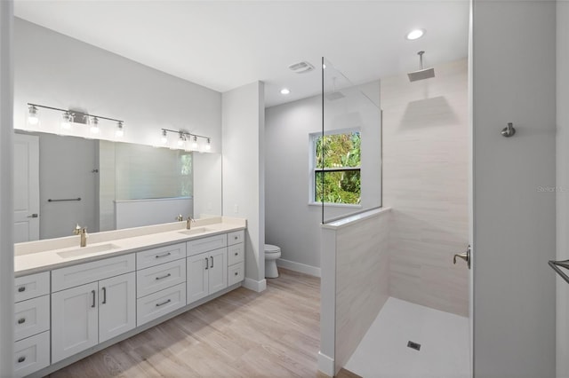 bathroom with vanity, toilet, hardwood / wood-style flooring, and tiled shower