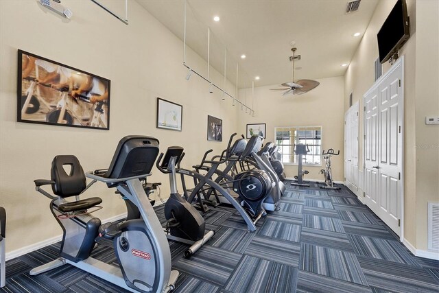 gym with a towering ceiling, ceiling fan, and dark carpet