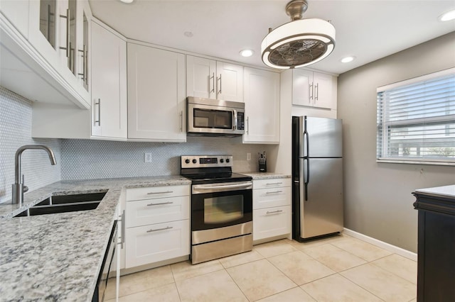 kitchen with appliances with stainless steel finishes, light stone countertops, decorative backsplash, sink, and white cabinets