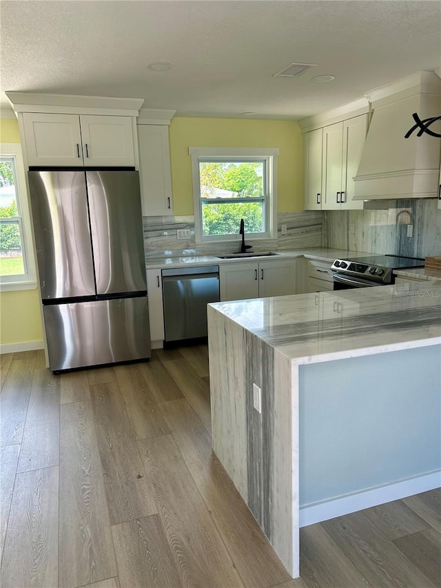 kitchen with sink, appliances with stainless steel finishes, light hardwood / wood-style flooring, white cabinets, and decorative backsplash