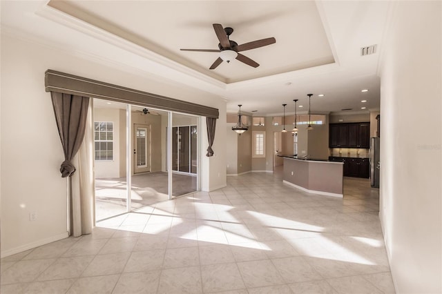 unfurnished living room with a raised ceiling, ceiling fan, light tile patterned flooring, and ornamental molding