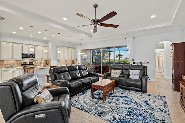 tiled living room featuring a raised ceiling, ceiling fan, and crown molding