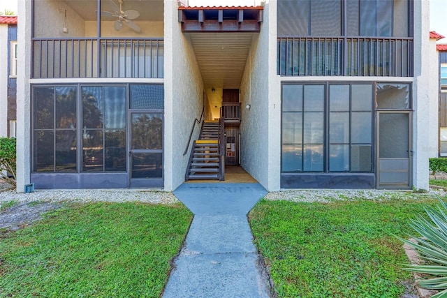 entrance to property with a balcony, a yard, and ceiling fan