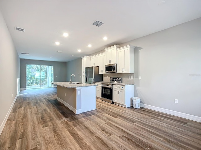 kitchen with white cabinetry, a center island with sink, appliances with stainless steel finishes, light stone countertops, and hardwood / wood-style floors