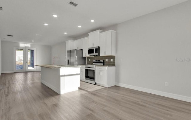 kitchen with french doors, light hardwood / wood-style flooring, a center island with sink, white cabinets, and appliances with stainless steel finishes