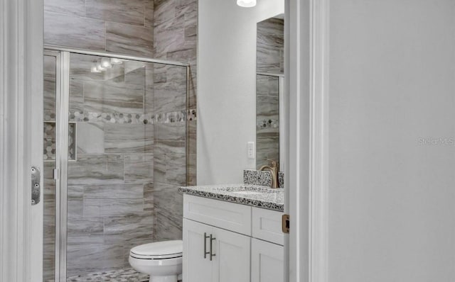 bathroom featuring a shower with door, vanity, and toilet