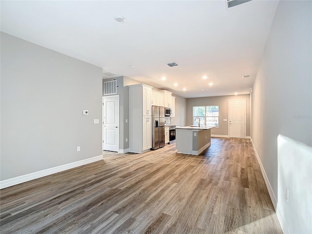 kitchen with an island with sink, sink, white cabinets, stainless steel appliances, and light wood-type flooring