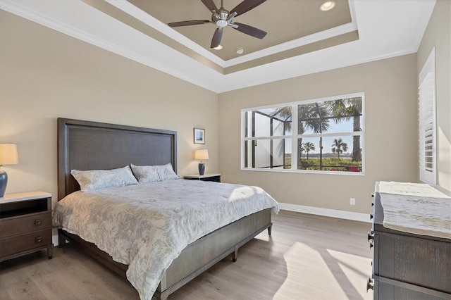 bedroom with ceiling fan, ornamental molding, a tray ceiling, and light wood-type flooring